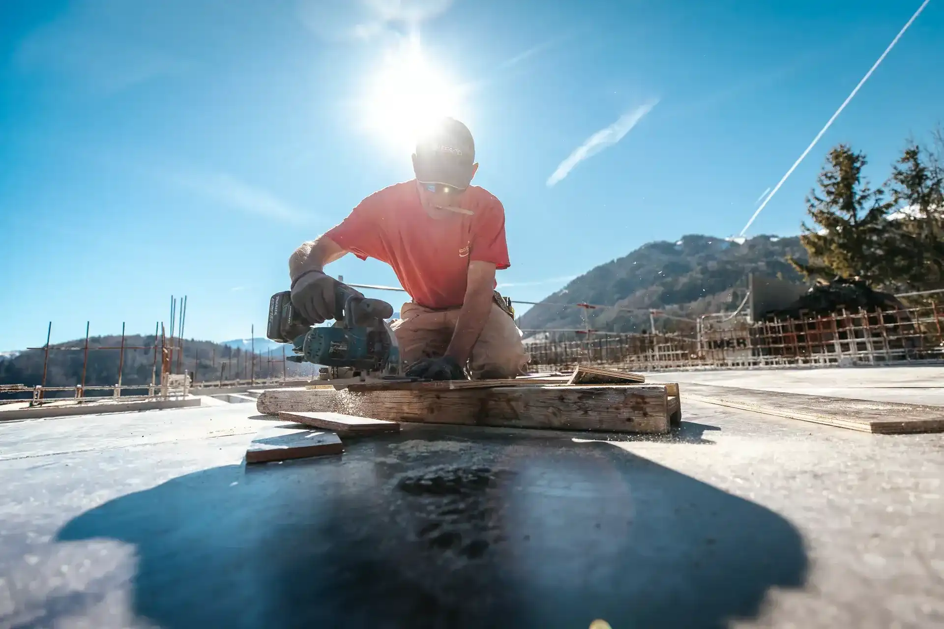 Maçon réalisant des finitions au sol, en contre-jour sur les montagnes