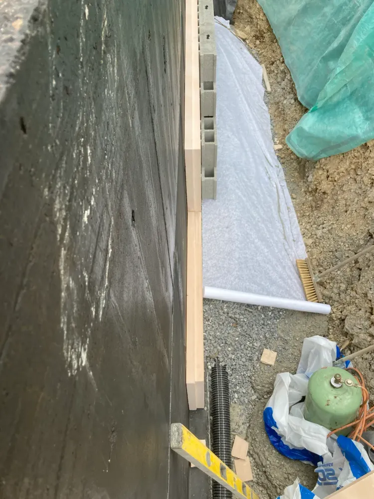 Étanchéité, isolant et blocs de drainage le long d'un mur enterré, géotextile déroulé sur le gravier