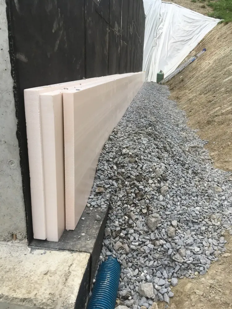 Panneaux isolants dressés contre l'étanchéité d'un mur de fondation, drain et remblai de gravier au pied
