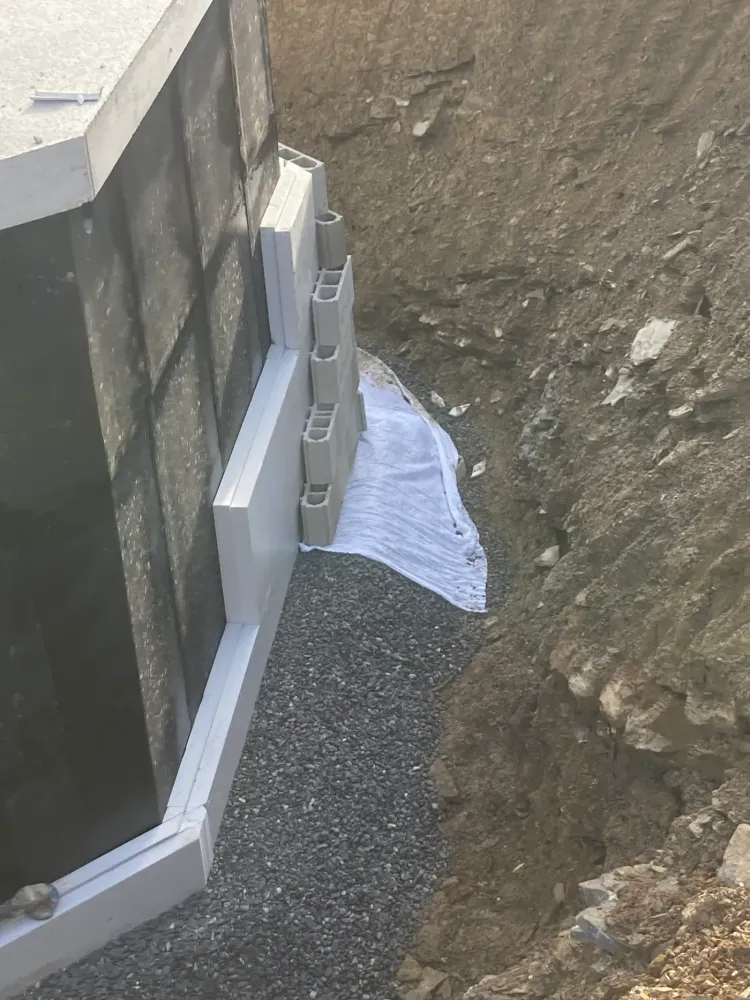 Blocs de drainage et isolant montés contre un mur de fondation étanchéifié, en fond de fouille