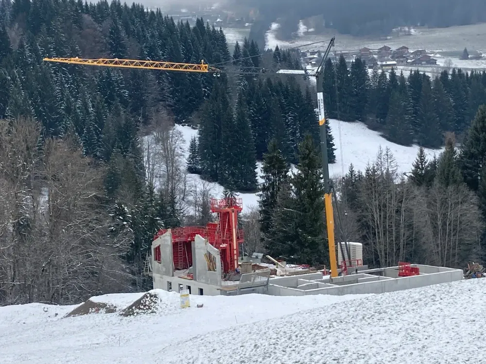 Chantier de gros œuvre sous la neige, grue à tour en fond de forêt